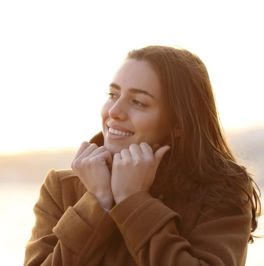 Happy woman in winter keeping warm grabbing jacket and looking away on the beach