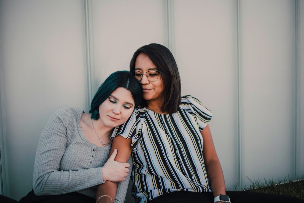 two women sitting side by side, one resting her head on the other's shoulder in a moment of quiet connection — repeating relationship patterns and attachment wounds couples therapy Oakland