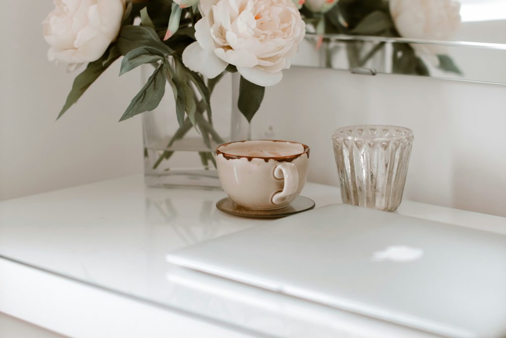 Calm white surface with a ceramic coffee cup, fresh peonies, and a glass candle holder, reflecting stillness and nervous system regulation therapy at Wildhaven Therapy Oakland
